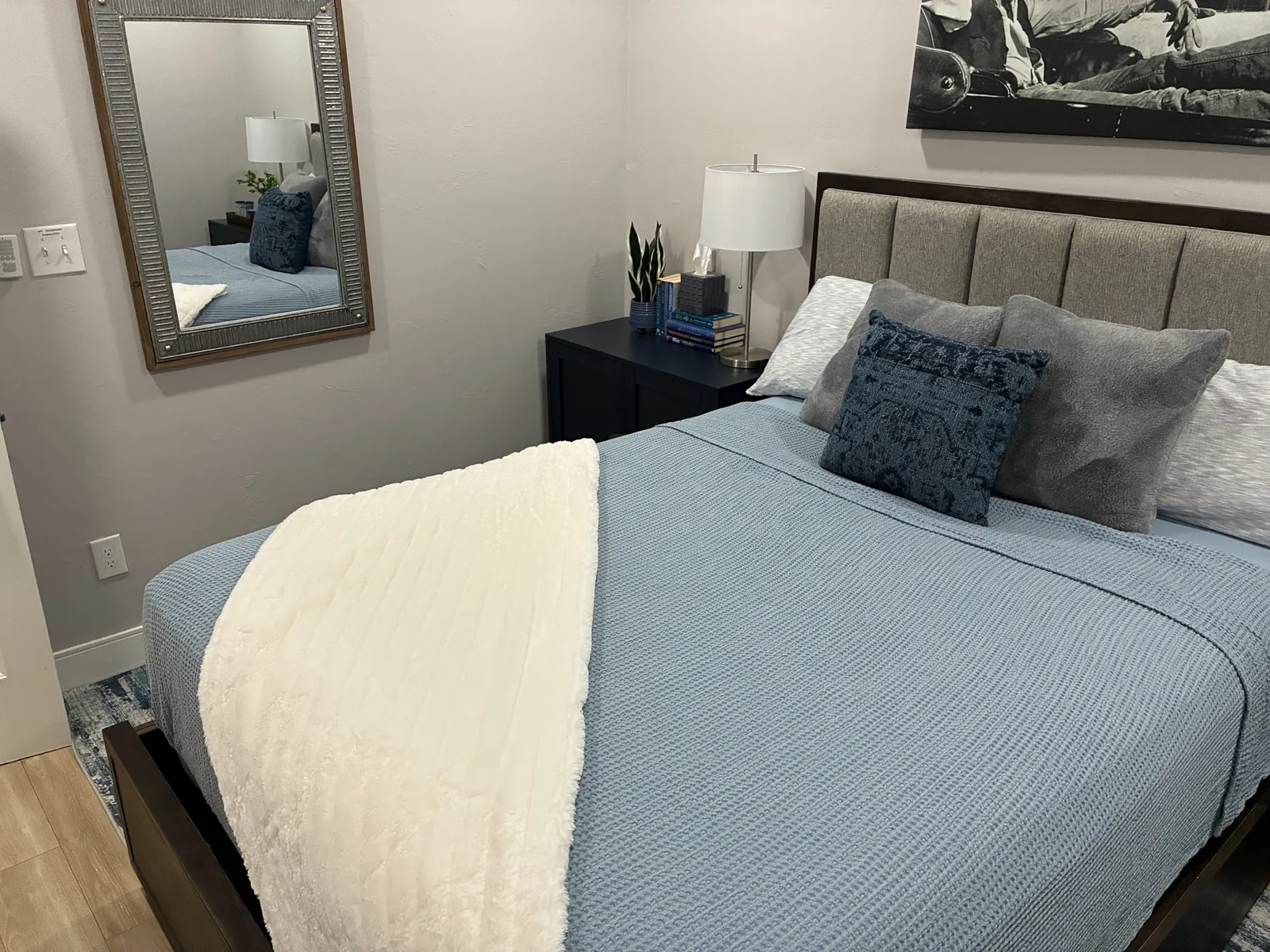 Neatly made bed with blue bedding, a white throw and a bedside table