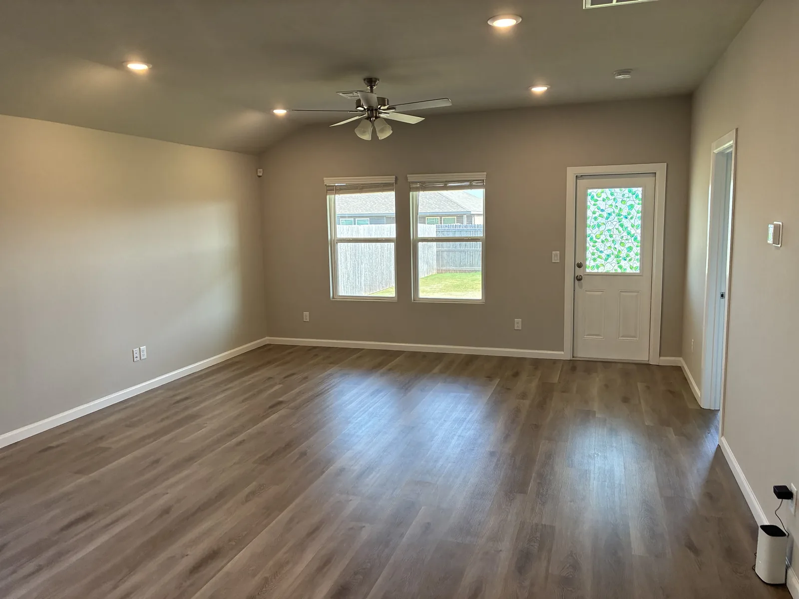 Empty living room with wood look flooring, windows and a back door