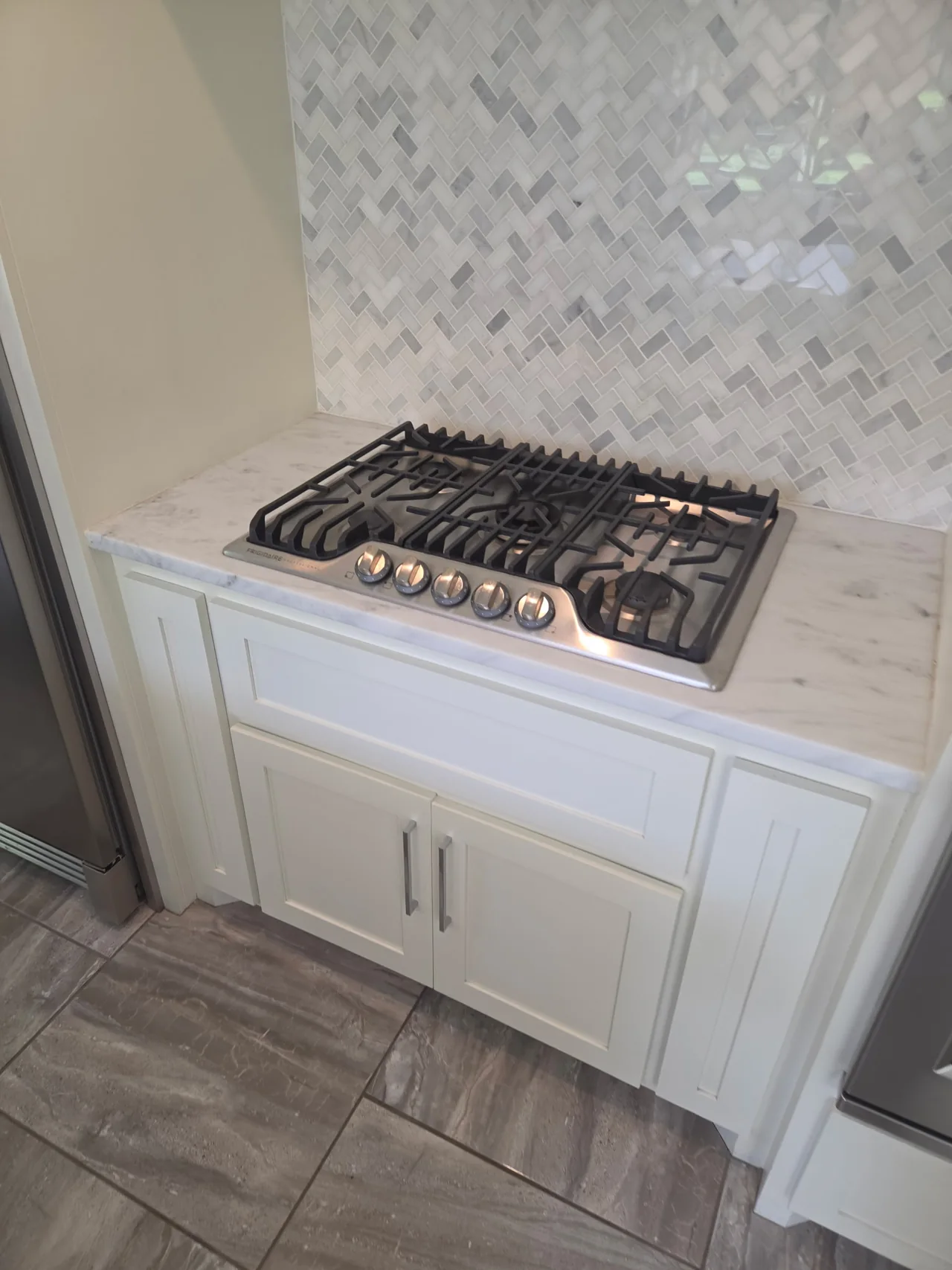 Gas cooktop with black grates, marble counter and tile backsplash