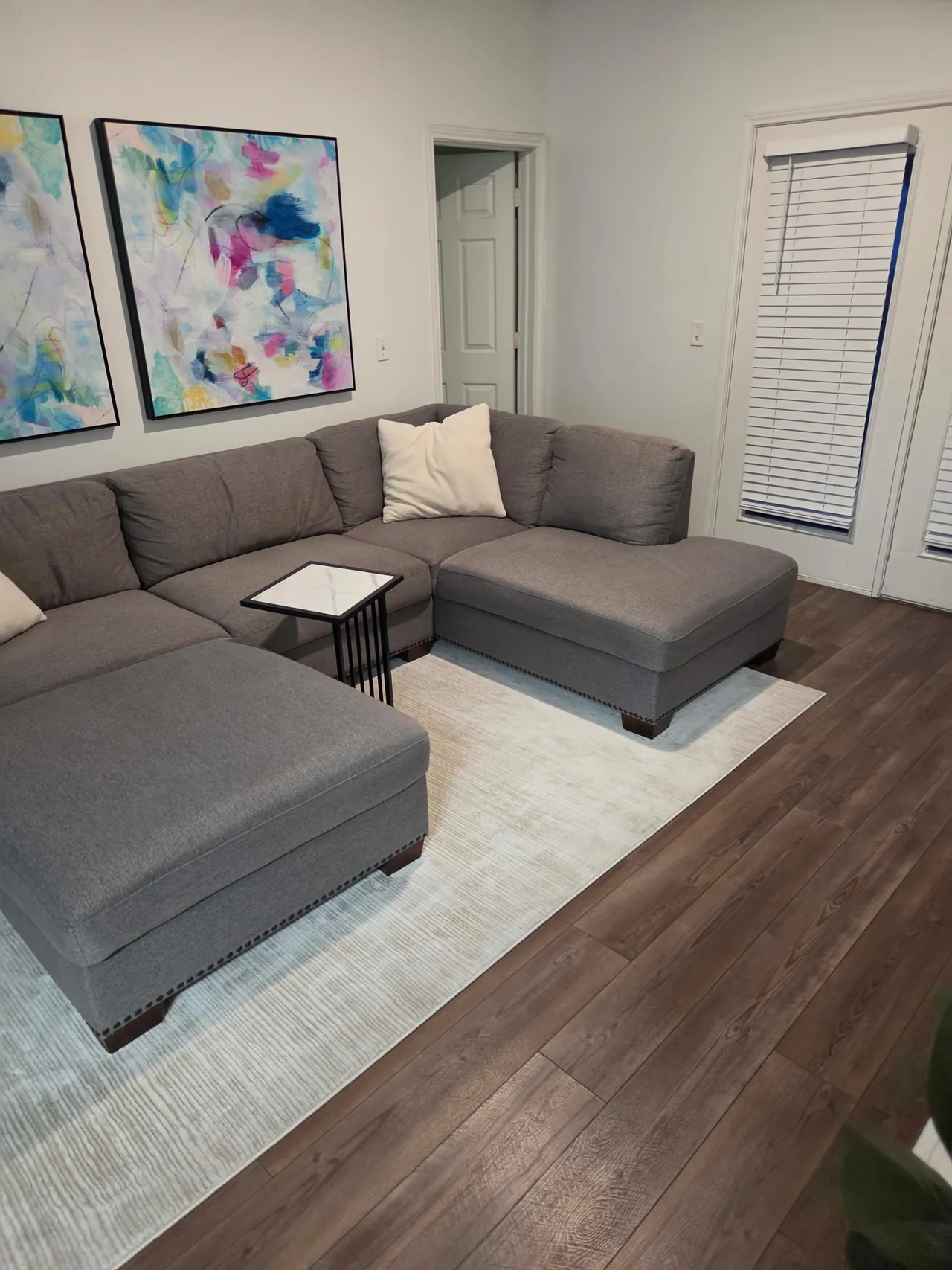Living room with a gray sectional, colorful artwork and clear wood look flooring