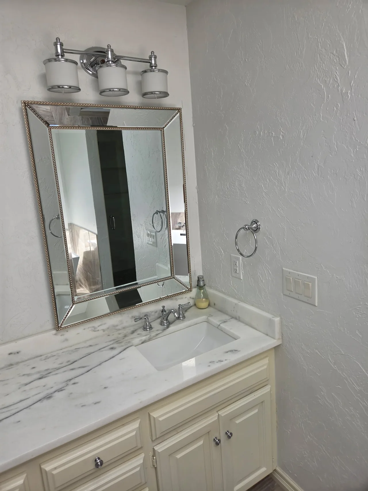 Bathroom vanity with a marble counter, chrome faucet and framed mirror