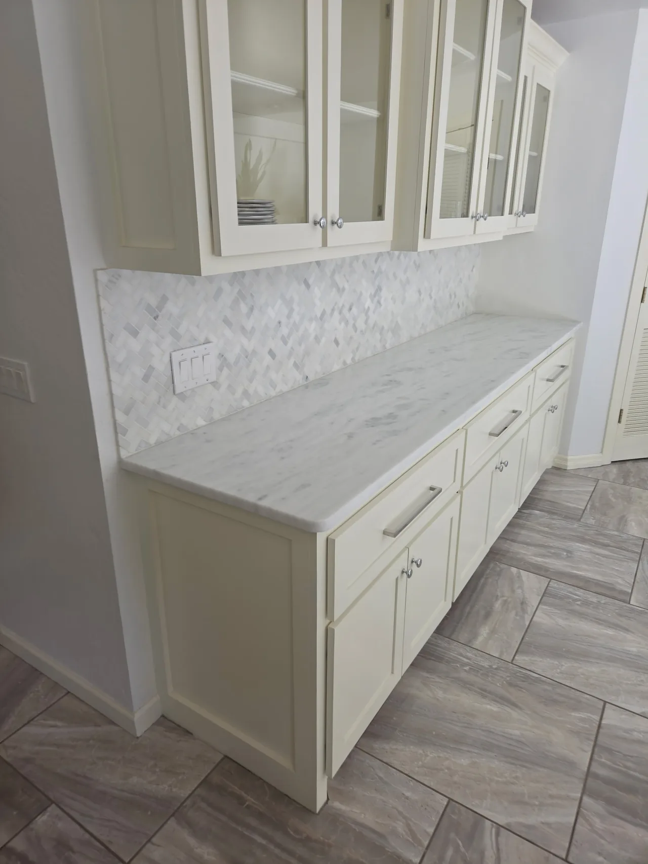 Cream kitchen cabinets with a clear marble counter and tile backsplash