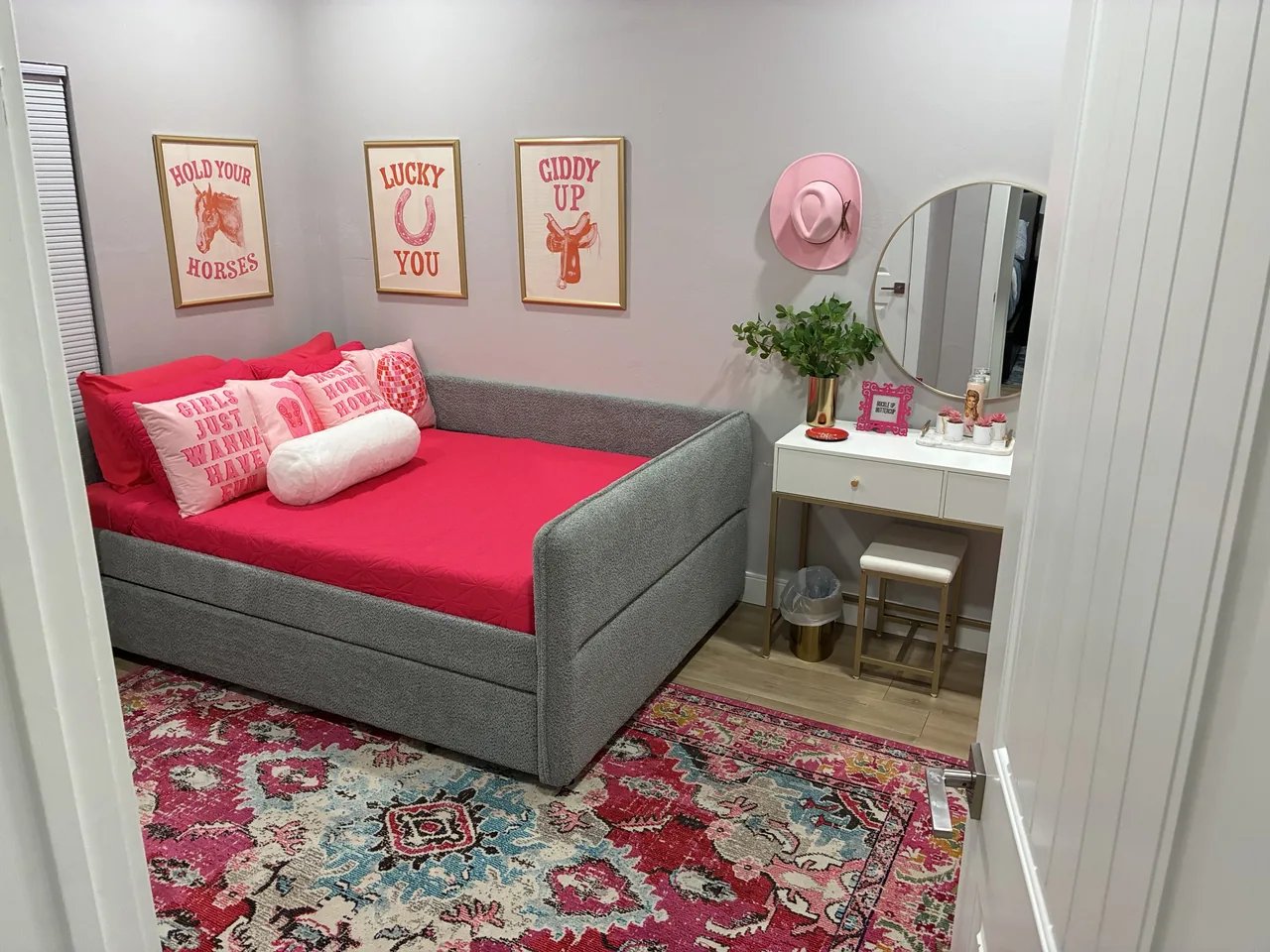 Bedroom with a gray daybed, pink bedding, white vanity and patterned rug