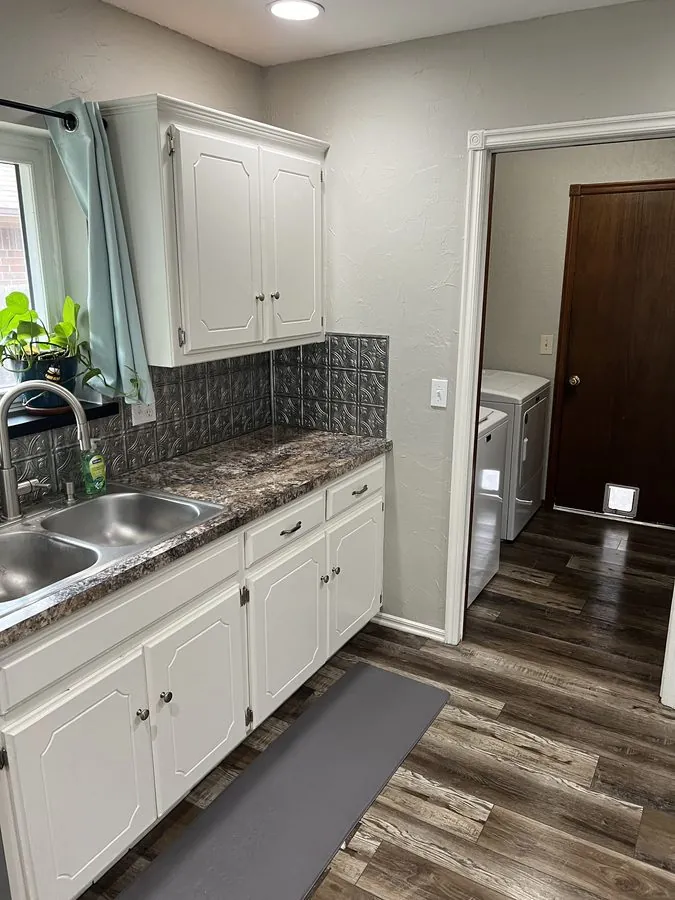 White kitchen cabinets and stainless sink beside a laundry doorway